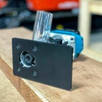 Black extended base plate for Makita trim router, shown installed on blue router with clear dust shield attached, view from front angle