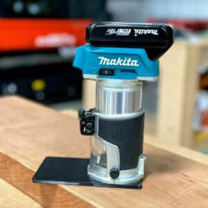 Black extended base plate mounted on a Makita cordless trim router standing on a wood board