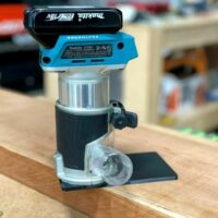 Makita XTR01 trim router mounted on extended base plate with black PETG platform, shown on wood workbench