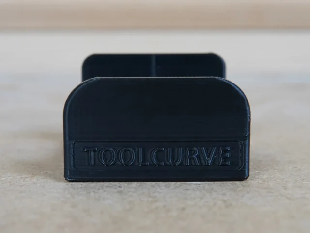 Black plastic headphone holder with ToolCurve branding, designed to slide into MFT/3 table t-track slot