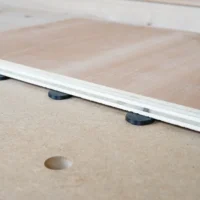 White plastic button protectors with black rubber pads sitting in 20mm bench dog holes on a wooden workbench