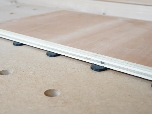 White plastic button protectors with black rubber pads sitting in 20mm bench dog holes on a wooden workbench