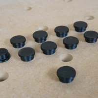 Nine black cylindrical button protectors and one with visible markings, displayed on a MFT workbench top with 20mm holes