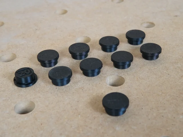 Nine black cylindrical button protectors and one with visible markings, displayed on a MFT workbench top with 20mm holes