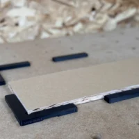 Black L-shaped bench dog fences marked 20mm on an MFT-style workbench, plywood panel held against them