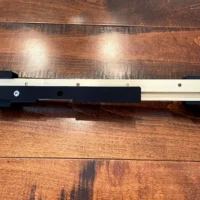 Narrow rip guide attached to Incra t-track rail with black plastic end stops and mounting hardware visible