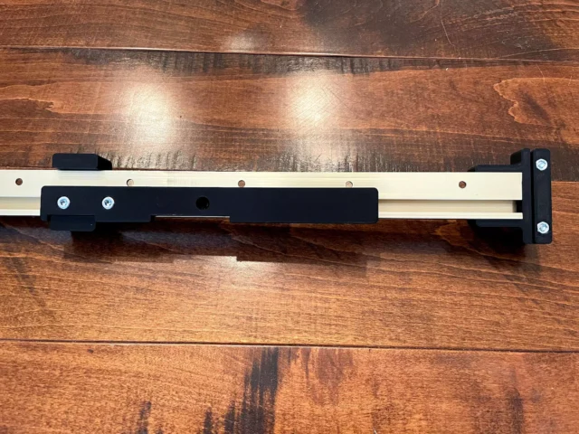 Narrow rip guide attached to Incra t-track rail with black plastic end stops and mounting hardware visible