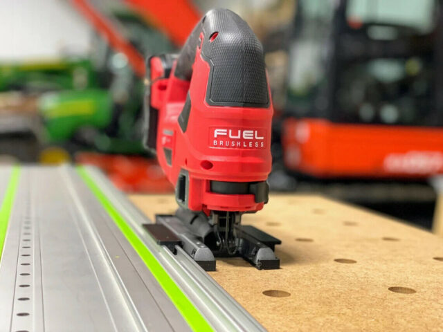 Milwaukee M18 jig saw with red FUEL body mounted on a green Festool rail via a snap-on adapter plate, showing the base connector