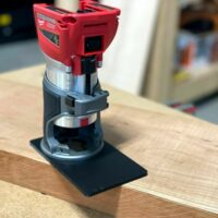Milwaukee trim router with extended black base plate sitting on wood, showing 120mm lengthened platform for stability