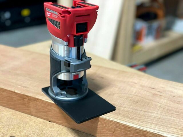 Milwaukee trim router with extended black base plate sitting on wood, showing 120mm lengthened platform for stability
