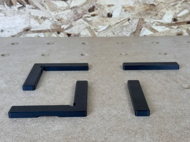 Four black corner and straight fence segments arranged on a perforated workbench surface