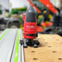 Red Milwaukee M18 jig saw adapter plate mounted on a Festool track rail, showing black snap-on base and dual rail connectors