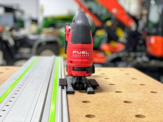 Red Milwaukee M18 jig saw adapter plate mounted on a Festool track rail, showing black snap-on base and dual rail connectors