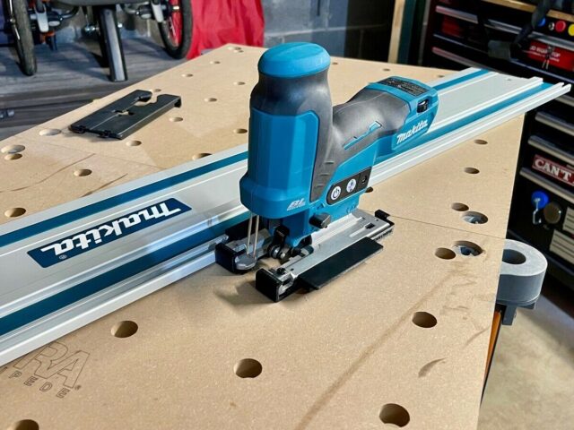Makita jigsaw mounted on blue and white track saw rail, showing black base plate adapter connecting the tool to the rail