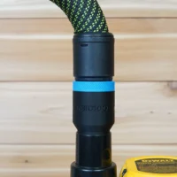 Black hose adapter with blue grip band attached to braided green hose, ToolCurve branding visible, mounted on Dewalt router