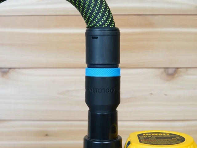 Black hose adapter with blue grip band attached to braided green hose, ToolCurve branding visible, mounted on Dewalt router