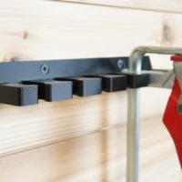 Quick Clamp Wall Mount Rack mounted on light wood, holding four Bessey clamps horizontally with a red clamp visible on the right