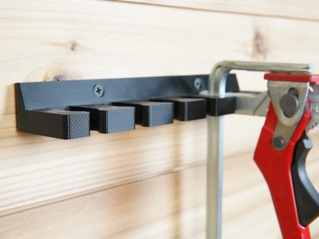 Quick Clamp Wall Mount Rack mounted on light wood, holding four Bessey clamps horizontally with a red clamp visible on the right