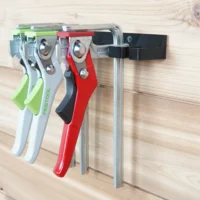 Black wall-mounted clamp rack screwed to a wood plank wall, holding three Festool and one red Bessey quick clamp