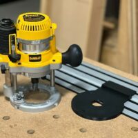 Dewalt DW618 plunge router mounted on black adapter plate connected to Dewalt track saw rail on wooden workbench with pegboard