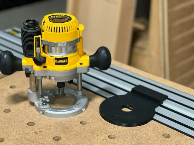 Dewalt DW618 plunge router mounted on black adapter plate connected to Dewalt track saw rail on wooden workbench with pegboard