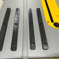 Four black miter bars lined up on a DeWalt table saw surface, each with three countersink holes for mounting
