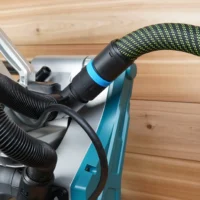 Black hose adapter with blue collar attached to Makita miter saw dust collection port, with black and lime green braided hose connected