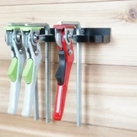 Quick clamp wall mount rack holding four Festool clamps with green and white handles and one red Bessey clamp, mounted on light wood wall