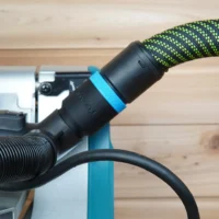 Black hose adapter with blue band attached to Makita miter saw dust port, connected to green and black hose