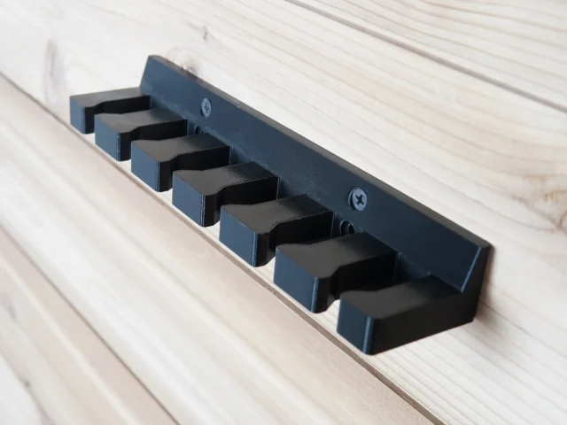 Blue quick clamp wall mount rack with six individual slots holding black clamp heads, mounted on white wood paneling