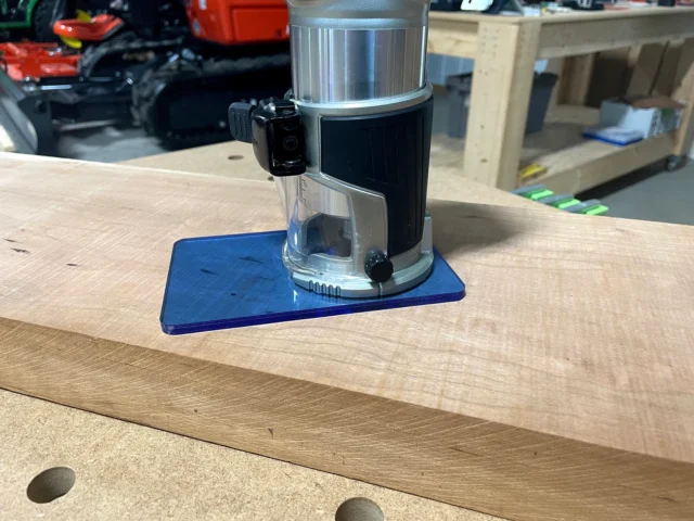 Blue transparent acrylic base plate mounted on a Makita trim router sitting on a wooden workbench