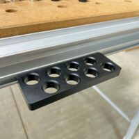 Black bench dog holder with eight circular holes mounted on a Festool MFT/3 aluminum t-track
