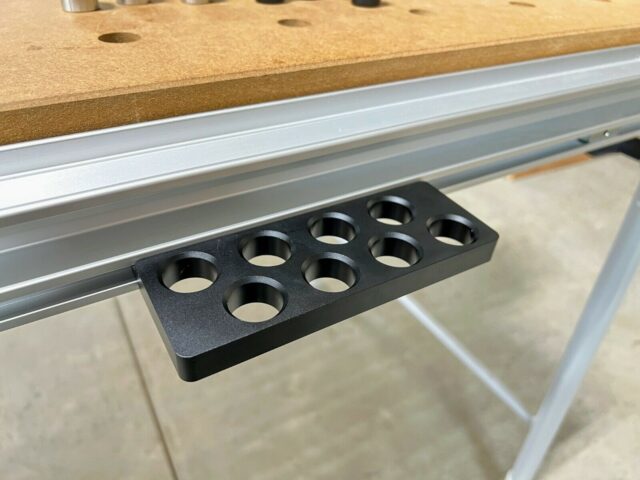 Black bench dog holder with eight circular holes mounted on a Festool MFT/3 aluminum t-track