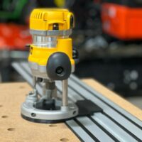 Dewalt DW618 plunge router mounted on aluminum track with black base plate, shown on wood workbench