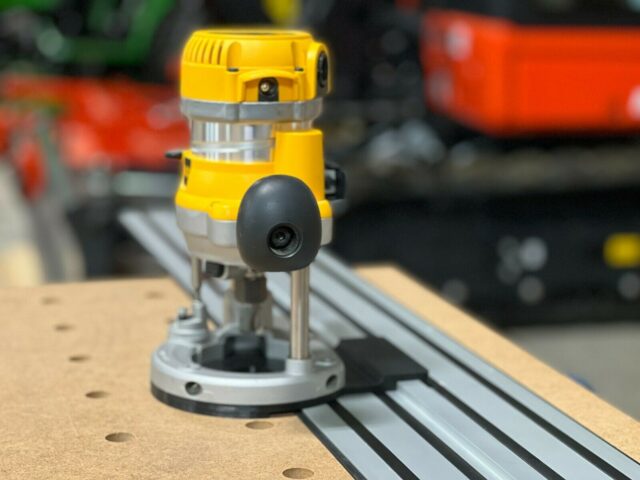 Dewalt DW618 plunge router mounted on aluminum track with black base plate, shown on wood workbench