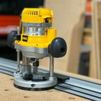 DeWalt DW618 plunge router mounted on DeWalt track saw rail, showing adapter base and router positioned for routing along the track