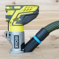 Black hose adapter with blue collar attached to the base of a Ryobi trim router, vacuum hose connected