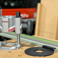 Bosch MR23EVS plunge router mounted on a guide rail adapter, shown from the side with a black baseplate in the foreground