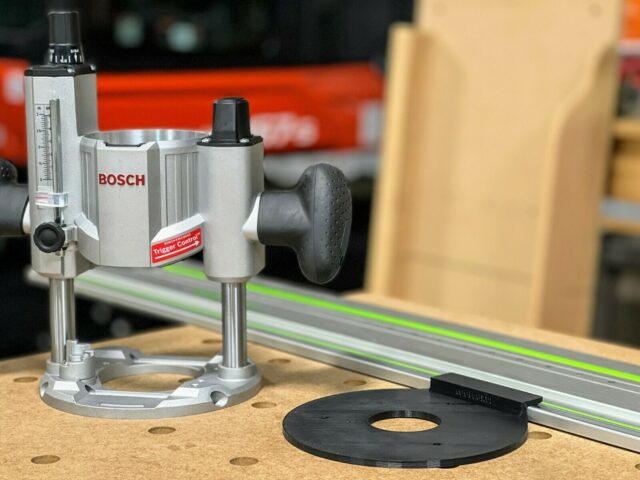 Bosch MR23EVS plunge router mounted on a guide rail adapter, shown from the side with a black baseplate in the foreground