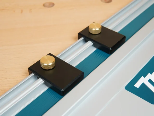Two black aluminum guide rail limit stops with brass knurled knobs mounted on Makita track saw rails