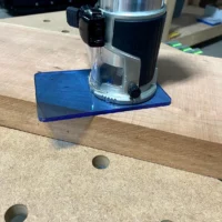 Blue transparent acrylic base plate mounted on a Makita trim router, shown on a wooden workbench