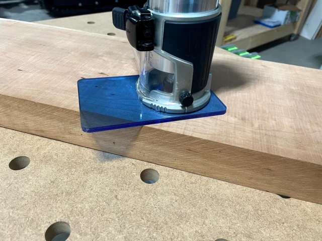Blue transparent acrylic base plate mounted on a Makita trim router, shown on a wooden workbench