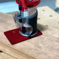 Red transparent acrylic base plate attached to a Milwaukee trim router on a wooden surface