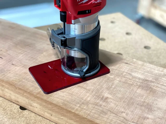 Red transparent acrylic base plate attached to a Milwaukee trim router on a wooden surface
