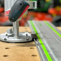 Bosch MR23EVS router adapter mounted on Festool guide rail, showing the black rubber handle grip and metal base plate positioned along the track