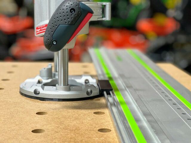 Bosch MR23EVS router adapter mounted on Festool guide rail, showing the black rubber handle grip and metal base plate positioned along the track