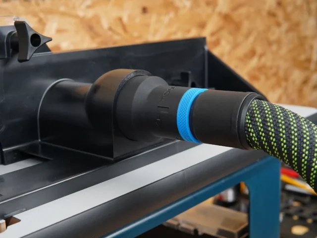 Black hose adapter with blue ring joining a green-flecked extractor hose to a router table dust port
