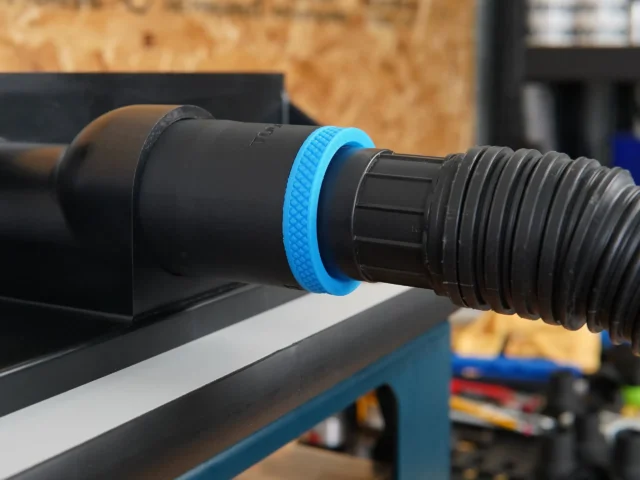 Blue hose adapter with threaded ports mounted on a router table dust collection port