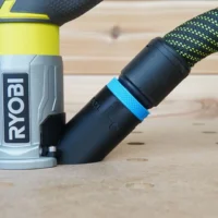 Black hose adapter with blue grip band attached to Ryobi trim router dust port on wood surface