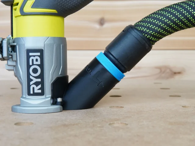 Black hose adapter with blue grip band attached to Ryobi trim router dust port on wood surface